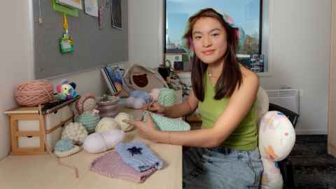 Victoria crochets at her desk while surrounding by many other crochet crafts. 