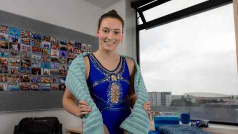 Chloe stands in her room wearing a sparkling competition swimsuit and a towel around her shoulders