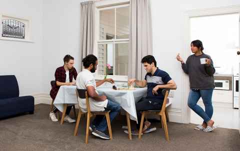 Group of four people in their flat around or near a table.