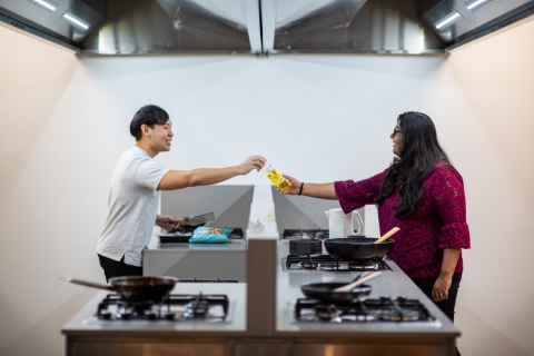 Two people in the shared kitchen at Te Tirohanga. They are cooking in their own sections while facing each other. One resident is handing something to the other over the middle barrier. 