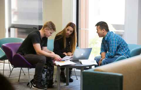 Three students huddles around a laptop and sitting 