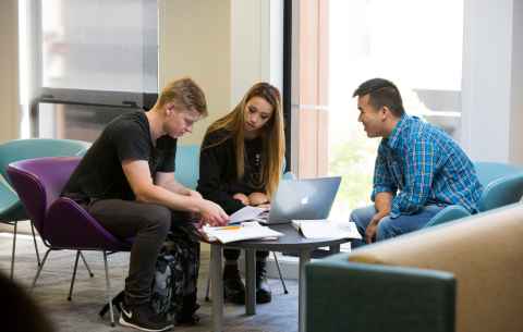 Three students huddled around a laptop and sitting