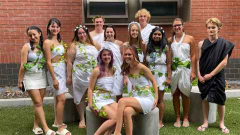 Medium sized group of people are gathered outside of Grafton Hall. They are dressed up in Toga-style clothing in preparation for Toga Night during Orientation Week. 