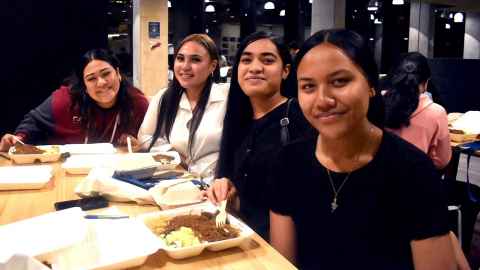 Four Pasifika students eat around a table and smile at the camera