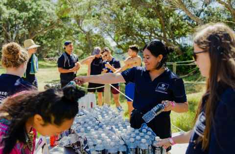 Two Resident Advisers hand out water bottles to residents in a park during an event. 