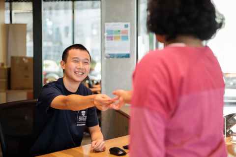 Staff member sitting behind a reception desk hands something to a visiting customer