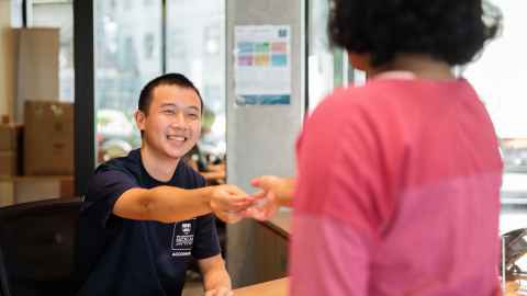 Staff member sitting behind a reception desk hands something to a visiting customer