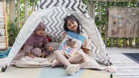 Two children in a tent, one poses with a book.
