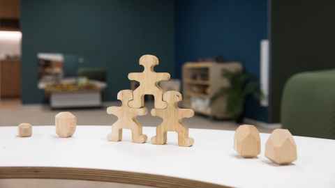 Three wooden blocks shaped like humans stacked on  top of each other in the foreground. 