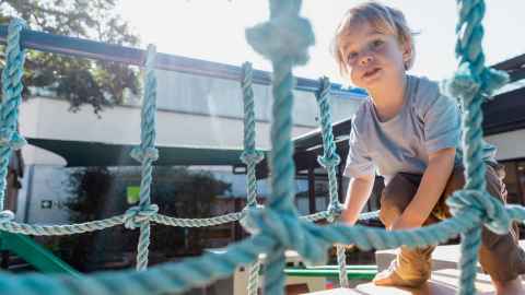 Child crosses playground bridge while squatting.