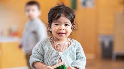 A little girl of preschool age, with another child in the background.