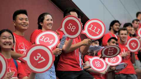 Group of students in red UniGuide t-shirts holding paddles, smiling and welcoming new students on Orientation day.