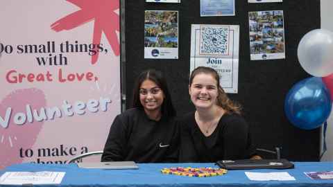 Two young women at a desk with signs displayed behind it saying 'Join' and Volunteer'.
