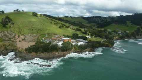 A group of buildings near a cliff, above crashing waves.