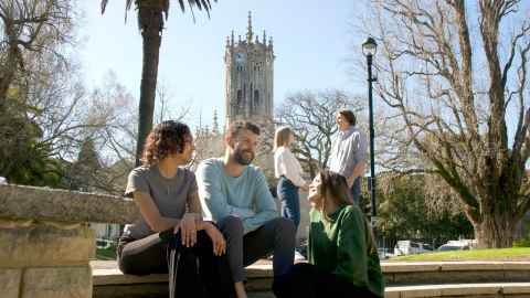 A group of people in a park on a sunny day with a clock tower behind them.