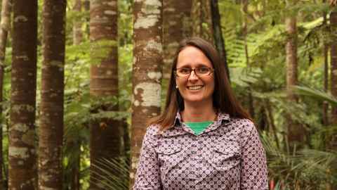 A dark-haired woman in glasses, with trees and ferns in the background.