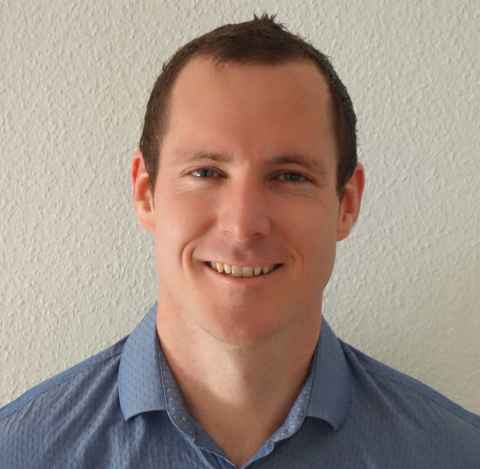 A smiling, dark-haired man in a blue shirt.