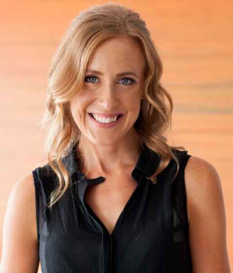A woman with fair, curly hair, smiling.