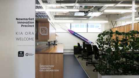 An office space with a welcome sign, bench, greenery, table and chairs.