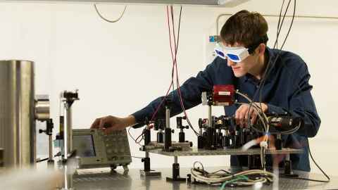 Physics student adjusting equipment in a lab wearing safety glasses