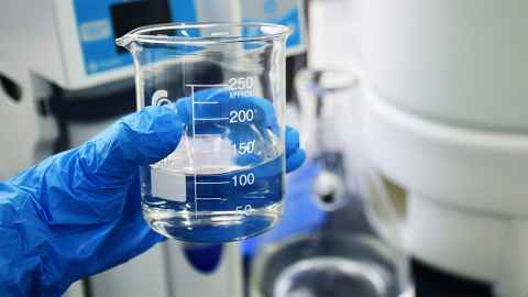 Hand holding a beaker with clear liquid. 