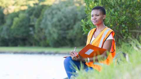 Student in high viz vest taking notes beside a river