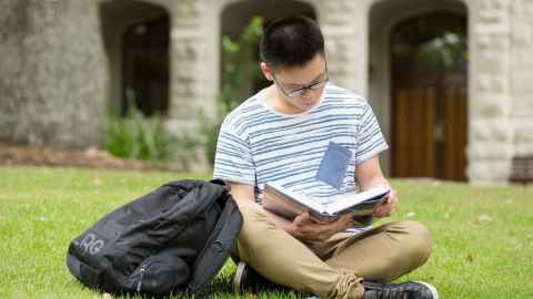 Student sitting and reading in campus lawn.