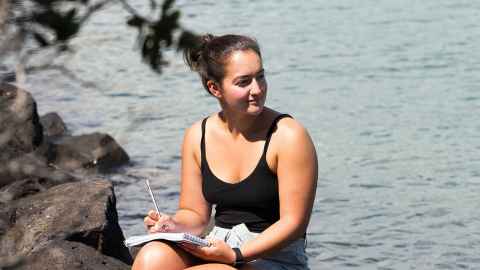 Female marine sciences student sitting on rocks by the water