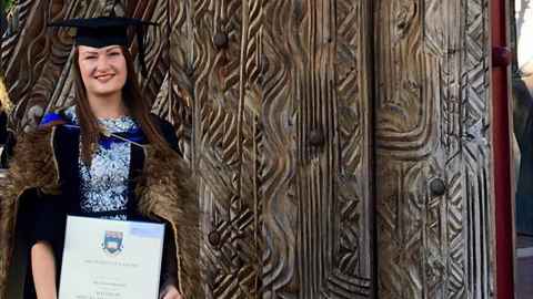 An image of Amy in her graduate cap and gown, holding her certificate