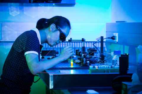 Medical physics student Fang Ou photographed in blue light wearing dark glasses working at a laboratory table