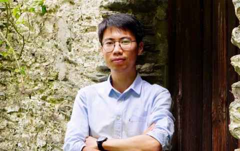 Research fellow Yang Chen posing against a brick wall background. 