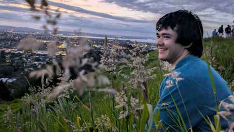 Science scholar Matt Illing standing against a pastel sunset background. 