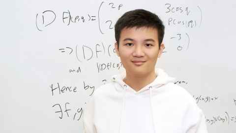 Science scholar Tristan Pang standing against a whiteboard background covered in mathematics equations. 