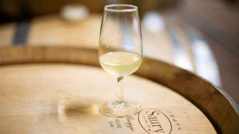 A glass of white wine sitting on top of a wine barrel