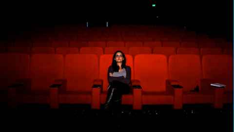 Ghazaleh Golbakhsh sitting at the centre of an empty cinema with red seats.