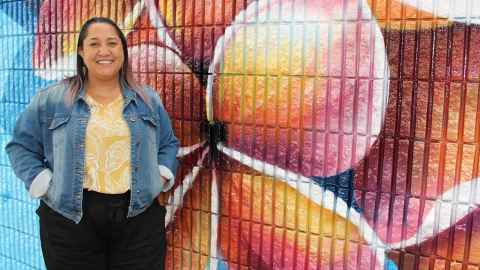 Jean stands smiling in front of a wall featuring beautiful frangipani graffiti.