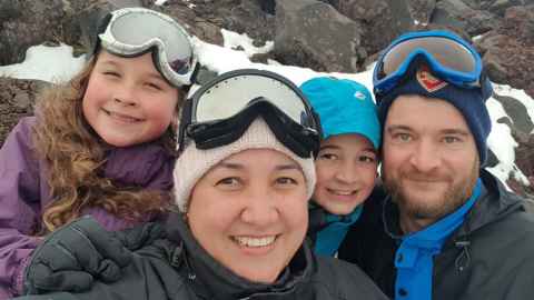 Jean, her daughter, son and husband stand grinning in front of snowy rocks.