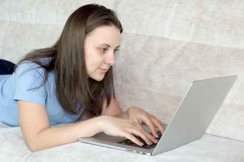 Student laying on a couch using their laptop. 