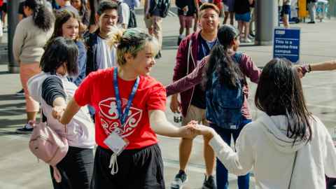 A group of students standing in a circle, holding hands.