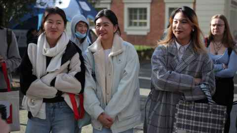 Group of new students in winter clothing. One female student with crossed arms smiling at camera. 