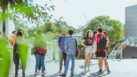 A group of students standing around, talking, near the Owen G Glenn building on the City Campus.