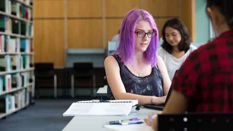 Girl with purple hair studying in library