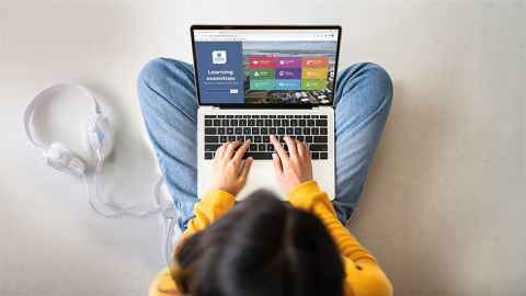 Top view of woman sitting on floor and using laptop with Learning essentials on screen.