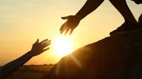 hands reaching out to touch each other with the sunset in the background