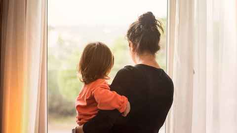 Parent holds child while looking out of a window
