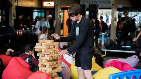 A young man stacking pieces of wood (like a game of Jenga) in the Quad.