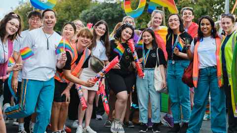 image of people at a pride march holding rainbow coloured "U.O.A" signs