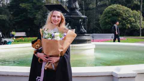 Sara Hall stands in Albert park smiling, holding a bunch of flowers