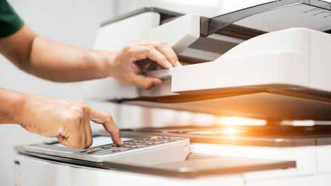 Hands opening a scanner lid and pressing buttons on a printer.