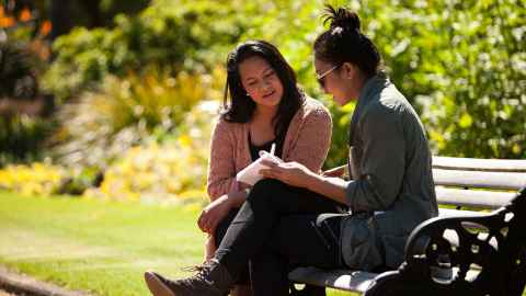 Two students sitting on a park bench in the sunshine